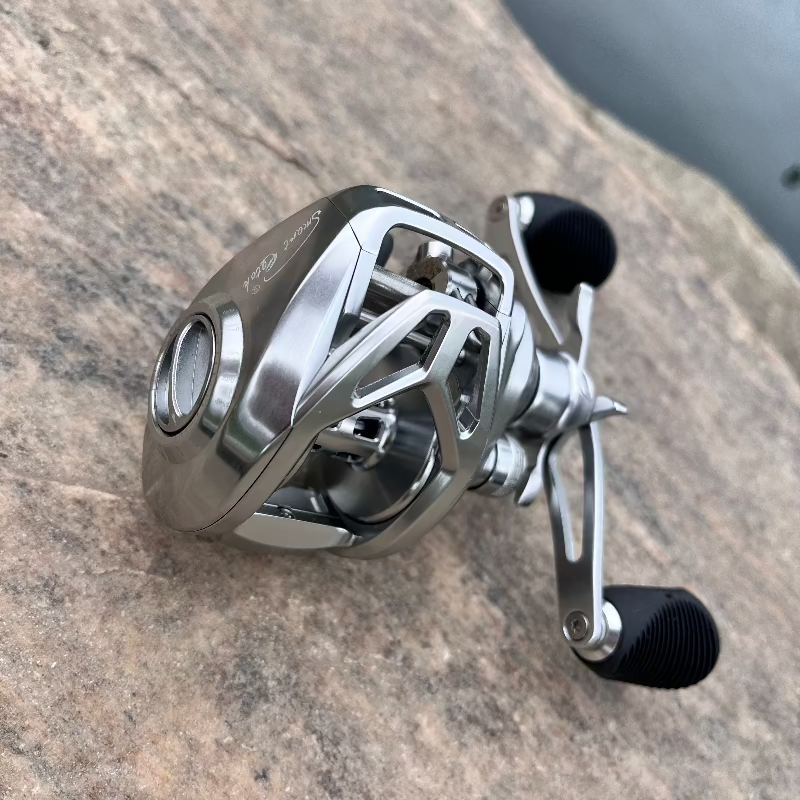 Angled view of the GOOFISH BCS250 silver reel on rock, showing the frame cutouts, spool and double handle