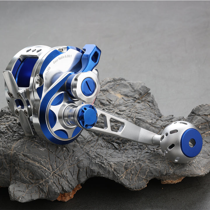 GOOFISH Abyss Jigger Gen 1 Blue and Silver reel on rock with its extended handle arm and perforated ball-style grip