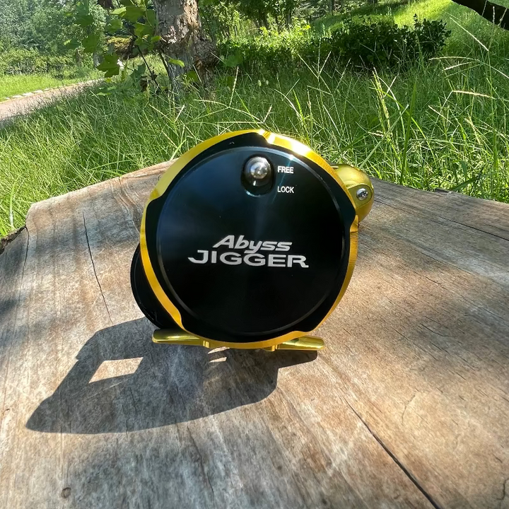 GOOFISH Abyss Jigger Gen 1 Navy Blue and Gold reel on a wooden surface, showing the sideplate and free-lock markings