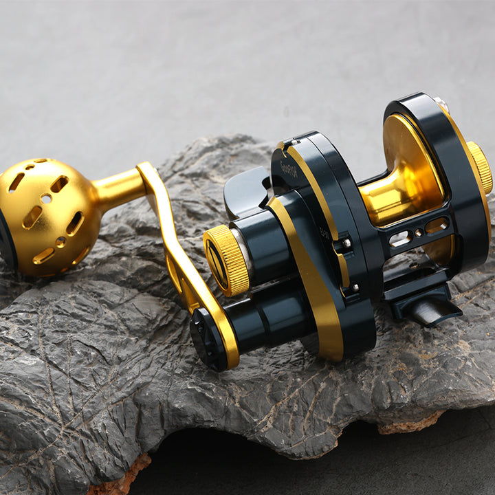 GOOFISH Abyss Jigger Gen 1 Navy Blue and Gold reel on rock, showing the gold spool and spherical metal grip